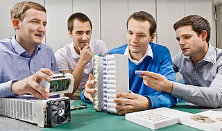 Die 4 Firmengründer von INVENOX sitzen am Tisch und begutachten ein Batteriesystem.mmen am Tisch.