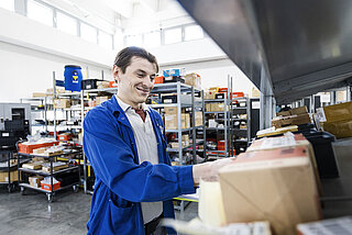 A man stands in front of a shelf and assembles production materials.