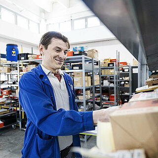 A man stands in front of a shelf and assembles production materials.